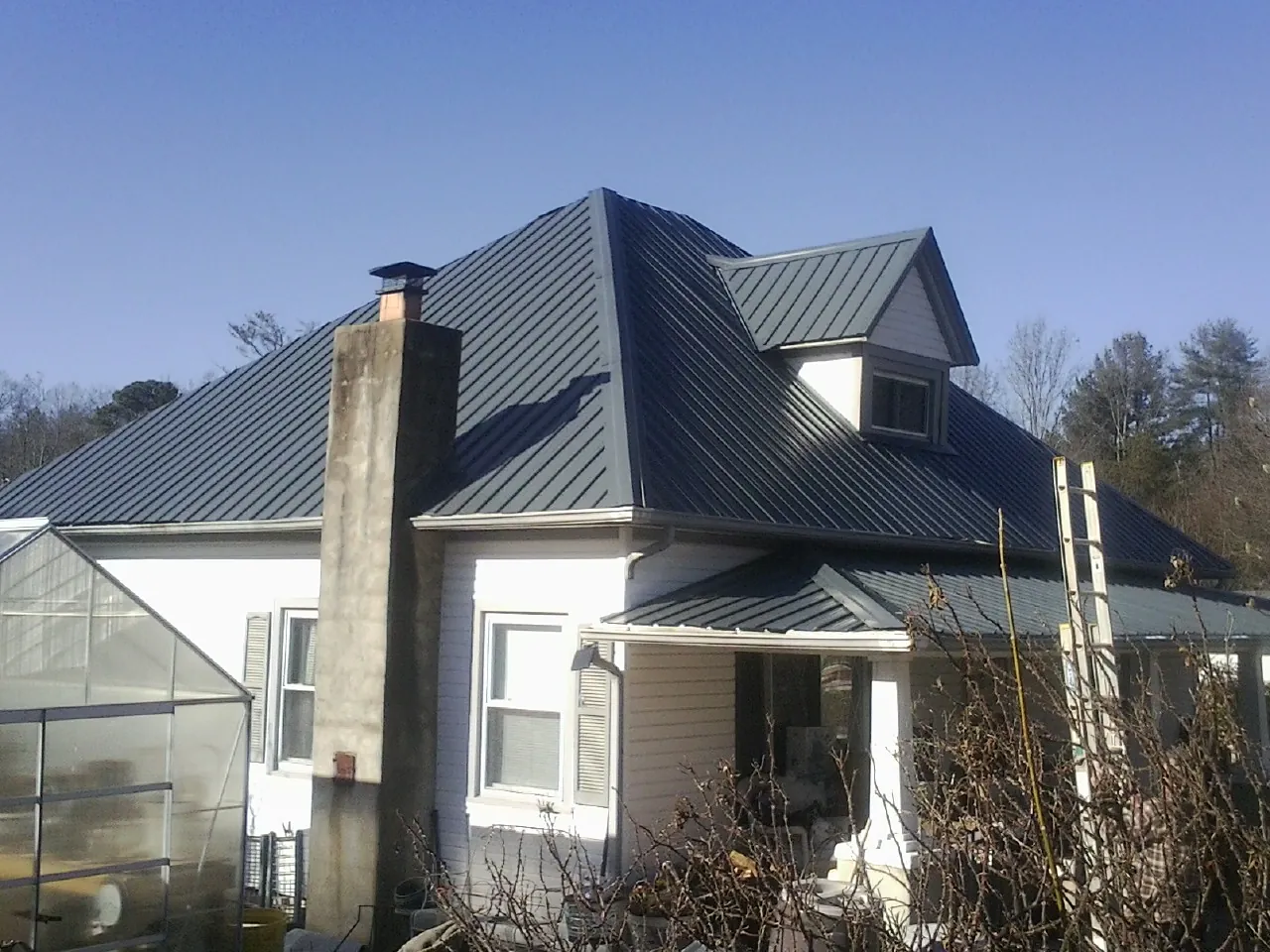 Dark blue standing seam metal roof on a white farmhouse with dormer in Janesville
