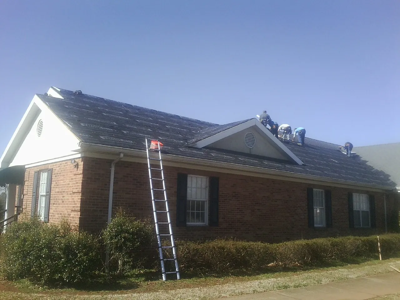 Crew tearing shingles off a brick ranch roof with a ladder set — Metal Roof Repair work by our crew in Janesville