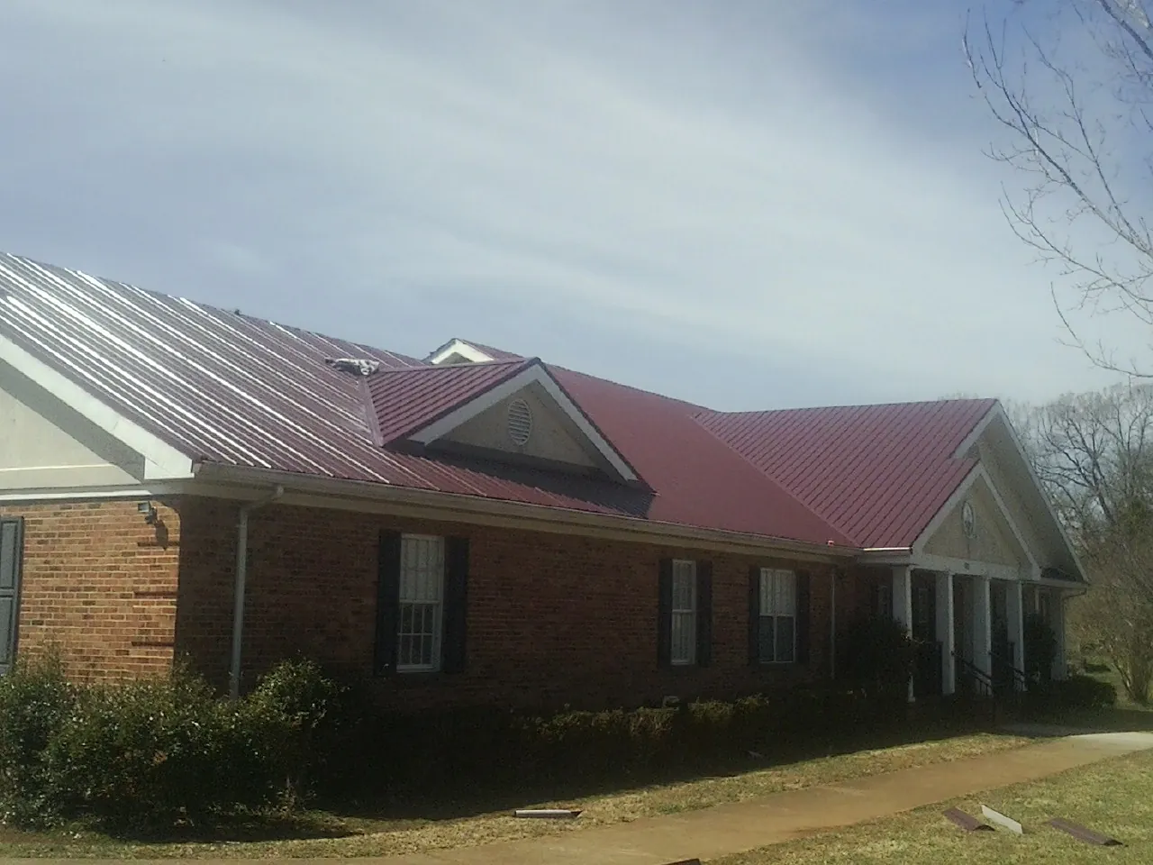 Red metal roof with gabled entries on a long brick building, from a Hail Damage Roof Repair job in Janesville