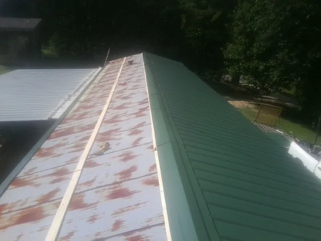 Old rusted panels beside newly installed green metal roofing — Wind Damage Roof Repair by Roofing Brothers in Janesville