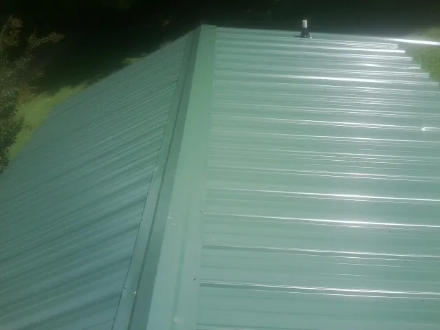 New green metal panels meeting at the ridge of a roof — Flat Roof Repair work by our crew in Janesville